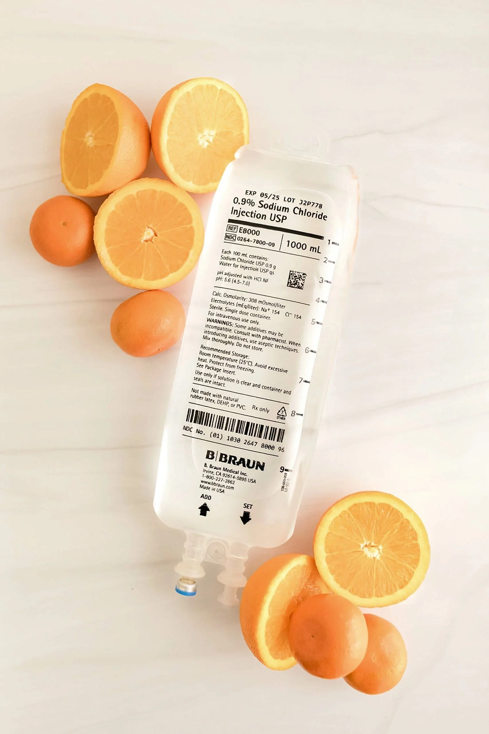 Syringe with a label for 0.9% Sodium Chloride Injection USP, surrounded by sliced oranges and whole oranges on a white surface.