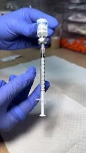 A person wearing blue gloves holding a syringe with a needle and a small vial attached.