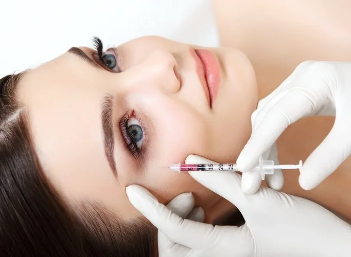 Woman receiving a cosmetic injection beneath her eye from a medical professional wearing white gloves.