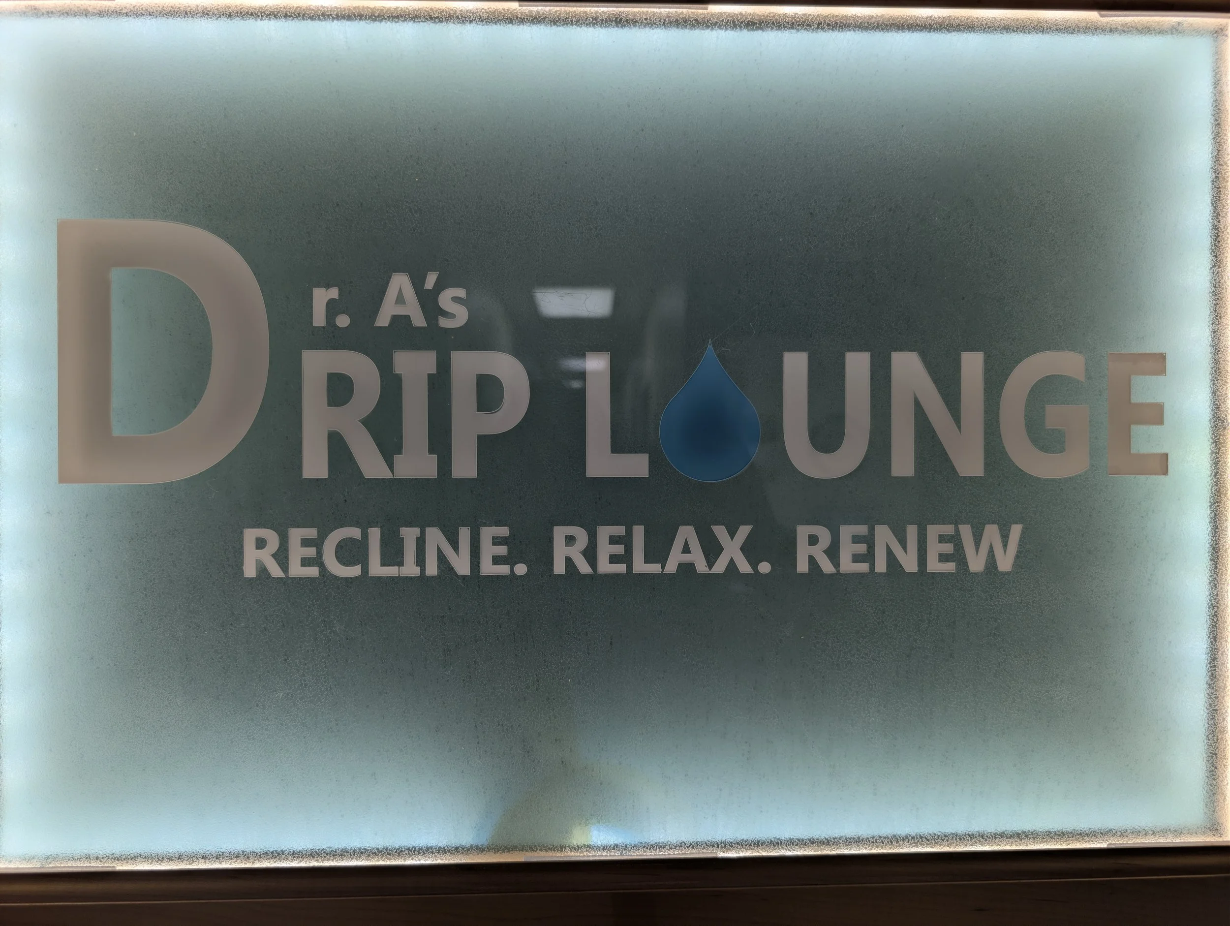 Signboard for r. A's Drip Lounge with the tagline RECLINE. RELAX. RENEW, featuring a blue water droplet in place of the letter 'I' in drip.
