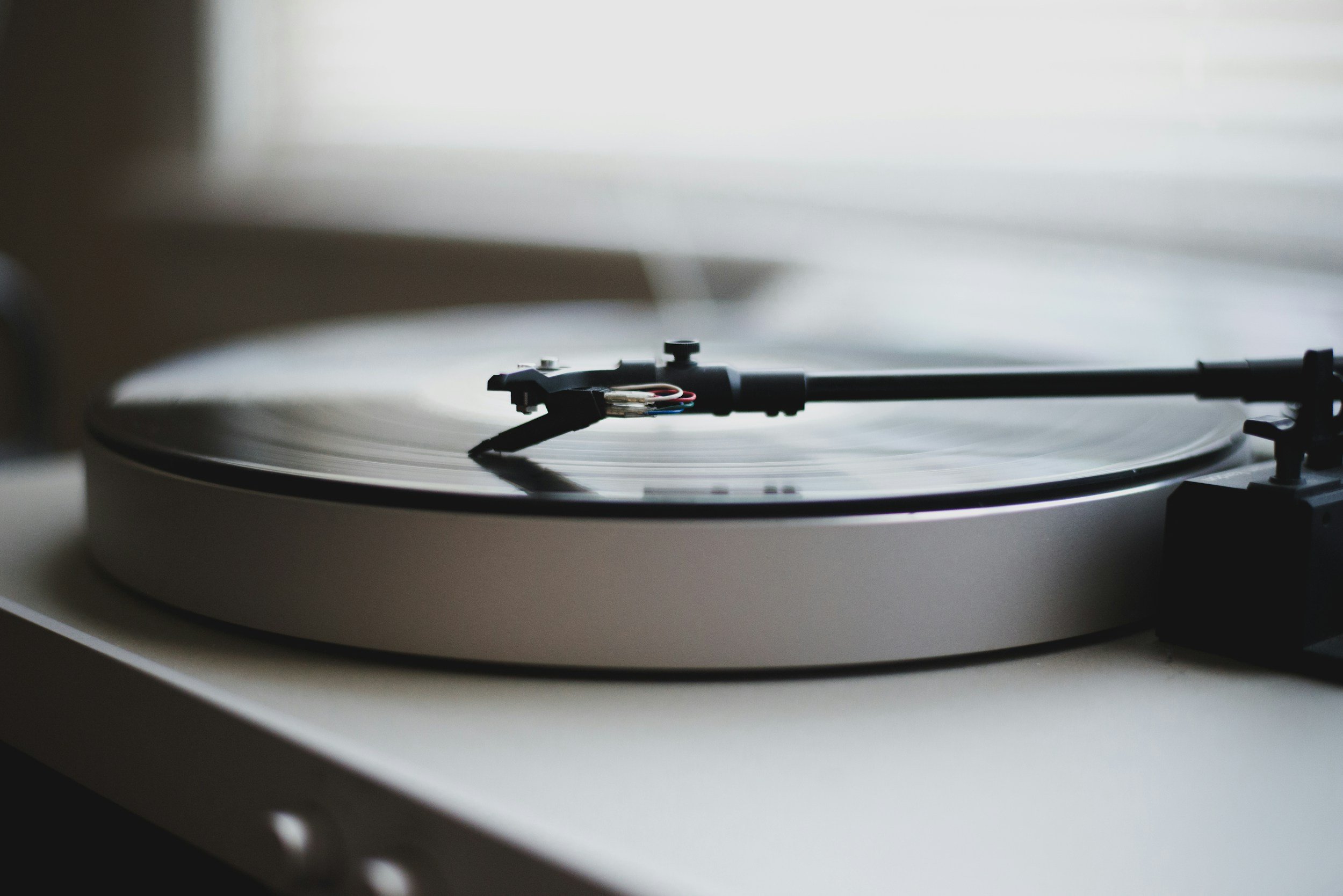 Close-up of a black turntable with a spinning vinyl record on a white surface, with a tonearm and stylus in position.