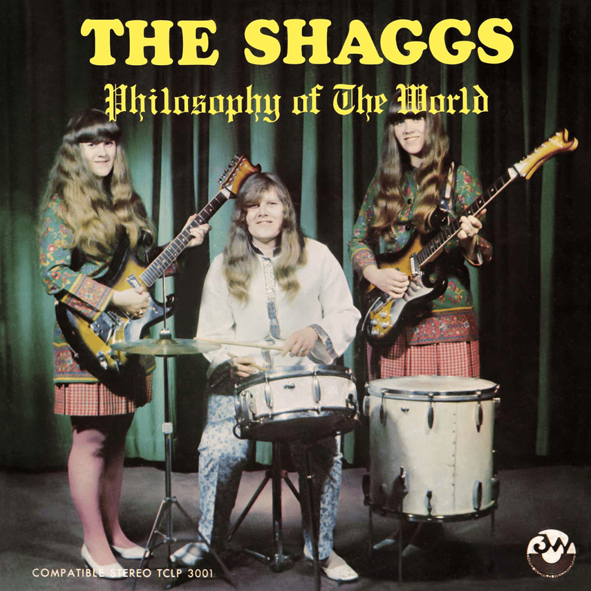 Album cover titled 'The Shaggs Philosophy of the World' featuring three young women in colorful vintage clothing with long hair, holding guitars and a drum set, standing in front of a dark curtain.