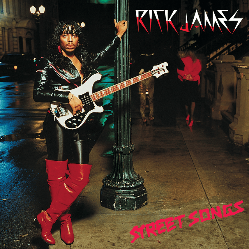 A person with long, curly hair and a leather jacket holding an electric guitar on a city street at night, with a woman in a pink coat in the background. The photo has the text 'Rick James' and 'Street Songs' on it.
