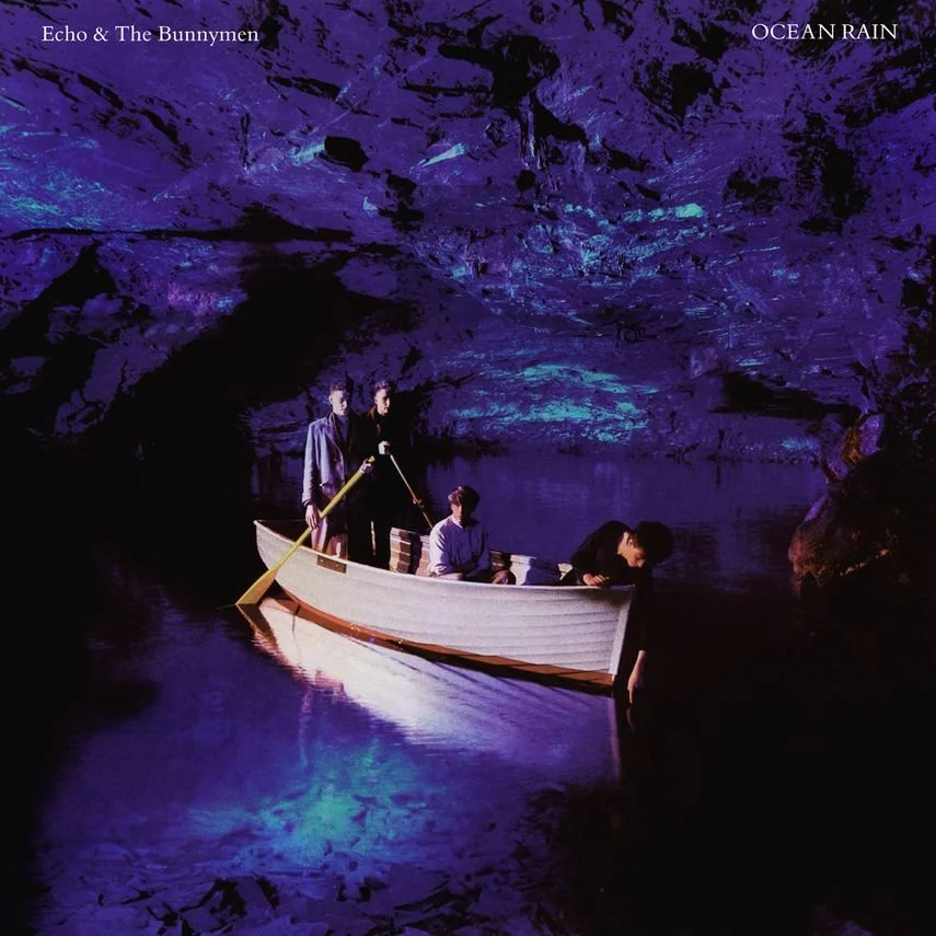 Four people in a boat on a dark, purple-lit waterway inside a cave with rocky walls.