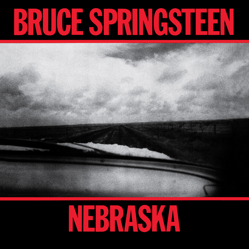 Black and white photo of a road through a rural landscape under cloudy sky, with bold red text at the top and bottom reading "Bruce Springsteen Nebraska."