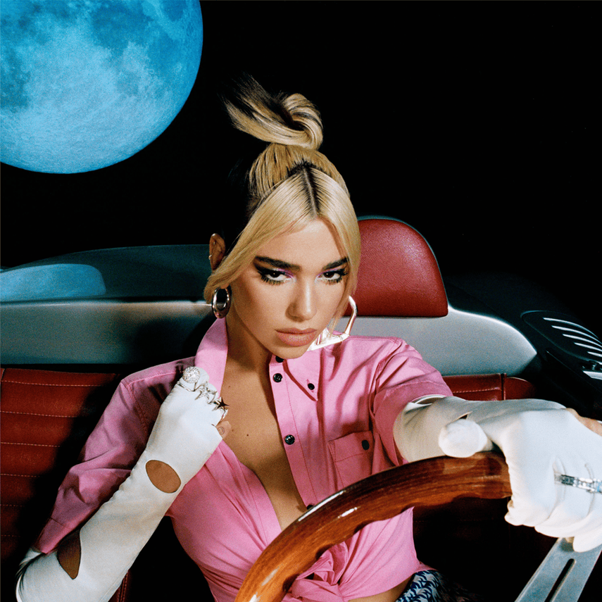 A woman with platinum blonde hair styled in a high ponytail, wearing a pink satin shirt, white gloves, and large hoop earrings, sitting in a vintage car with a red leather interior. The background features a large blue moon against a black night sky.