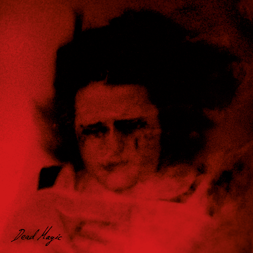 A reddish-toned photo of a person with dark hair and glasses, with the words 'Dead Magic' written in the bottom left corner.