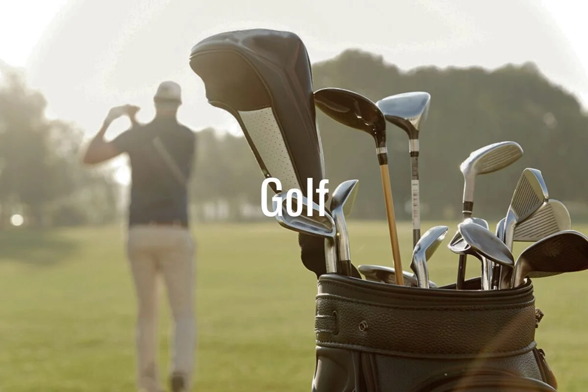 A golf bag with various golf clubs on a golf course with a golfer in the background adjusting his cap.