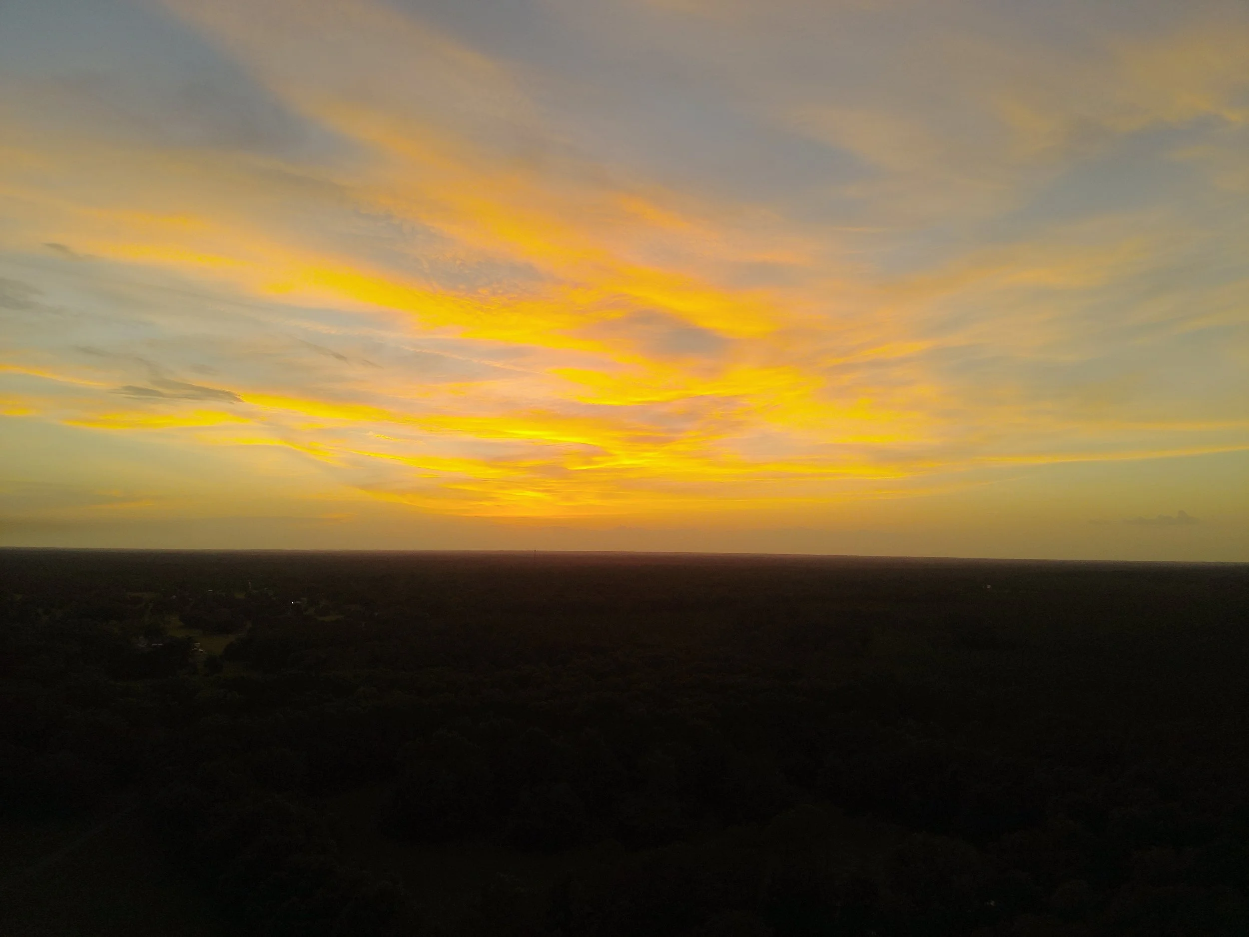 Sunset sky with colorful clouds over a dark landscape.