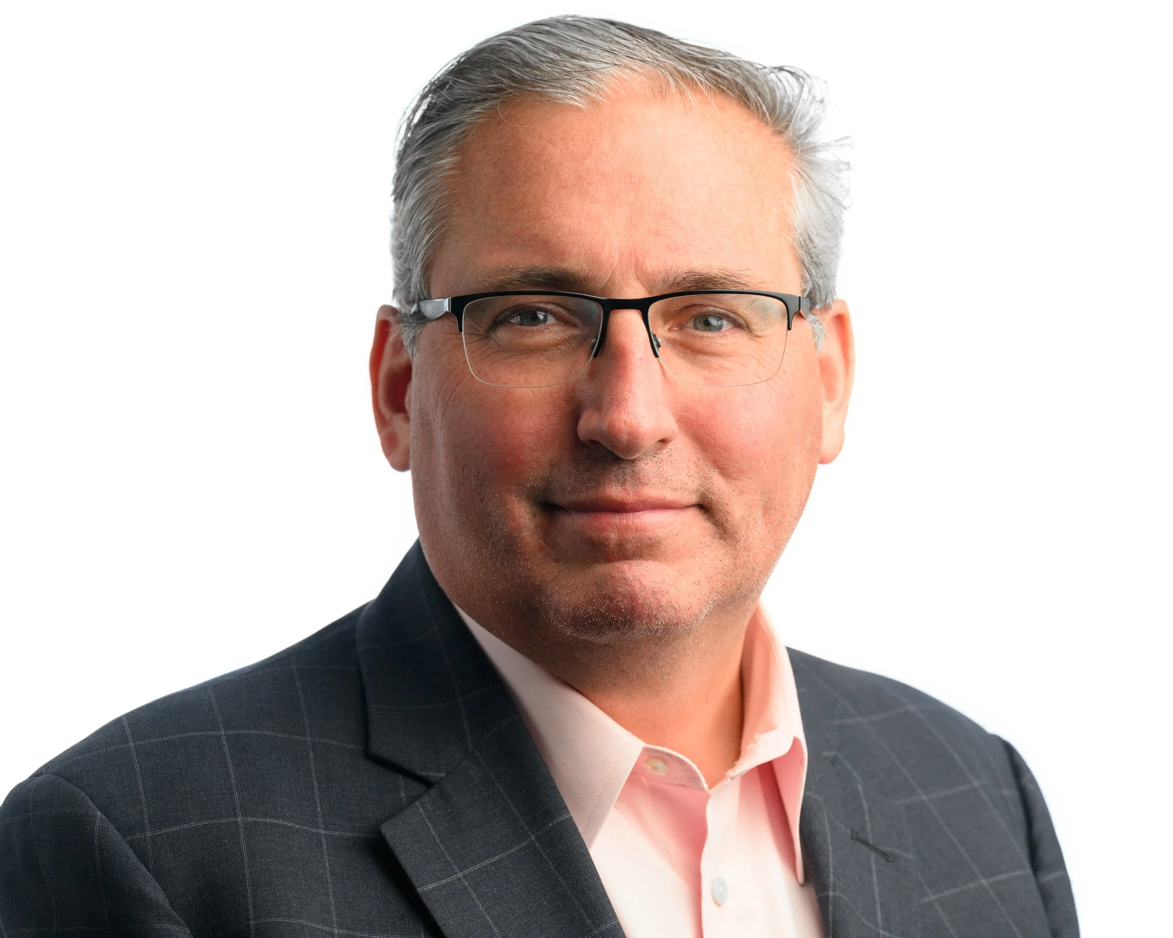 A middle-aged man with glasses, gray hair, and light skin, wearing a pink shirt and a dark plaid blazer, smiling confidently against a white background.
