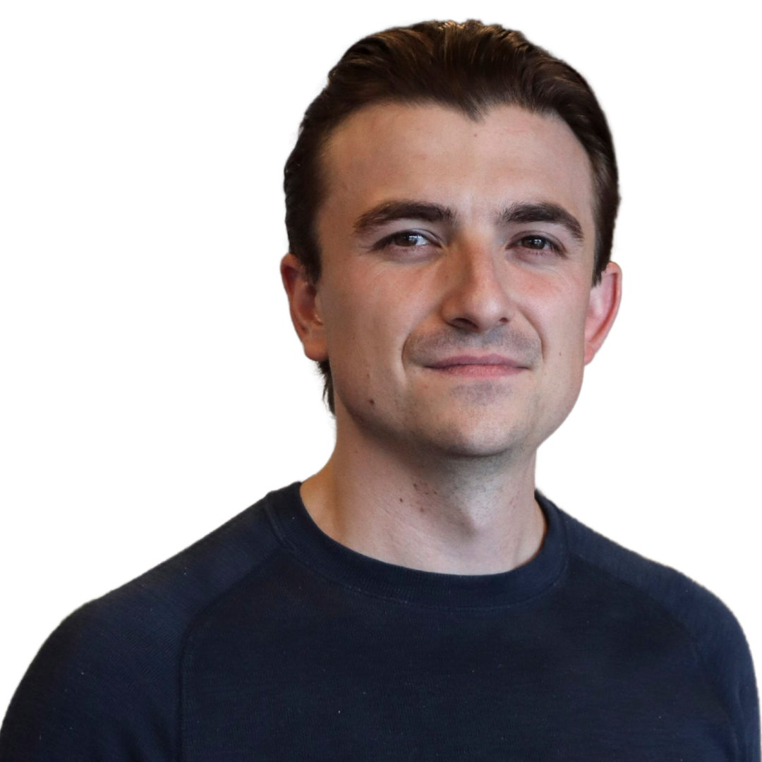A young man with short dark hair wearing a navy blue shirt, smiling slightly, against a plain white background.