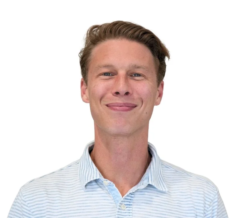 A young man with curly hair smiling in front of a white background.