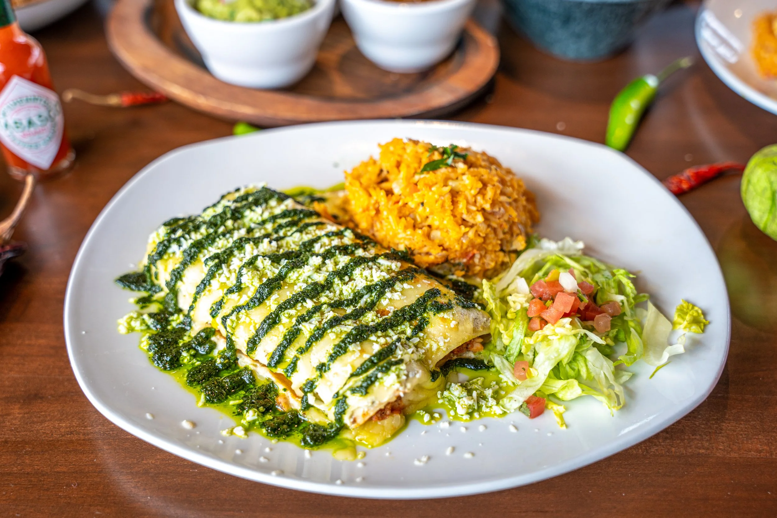 Plate with Mexican food including enchiladas topped with green sauce, Mexican rice, and a small side salad.