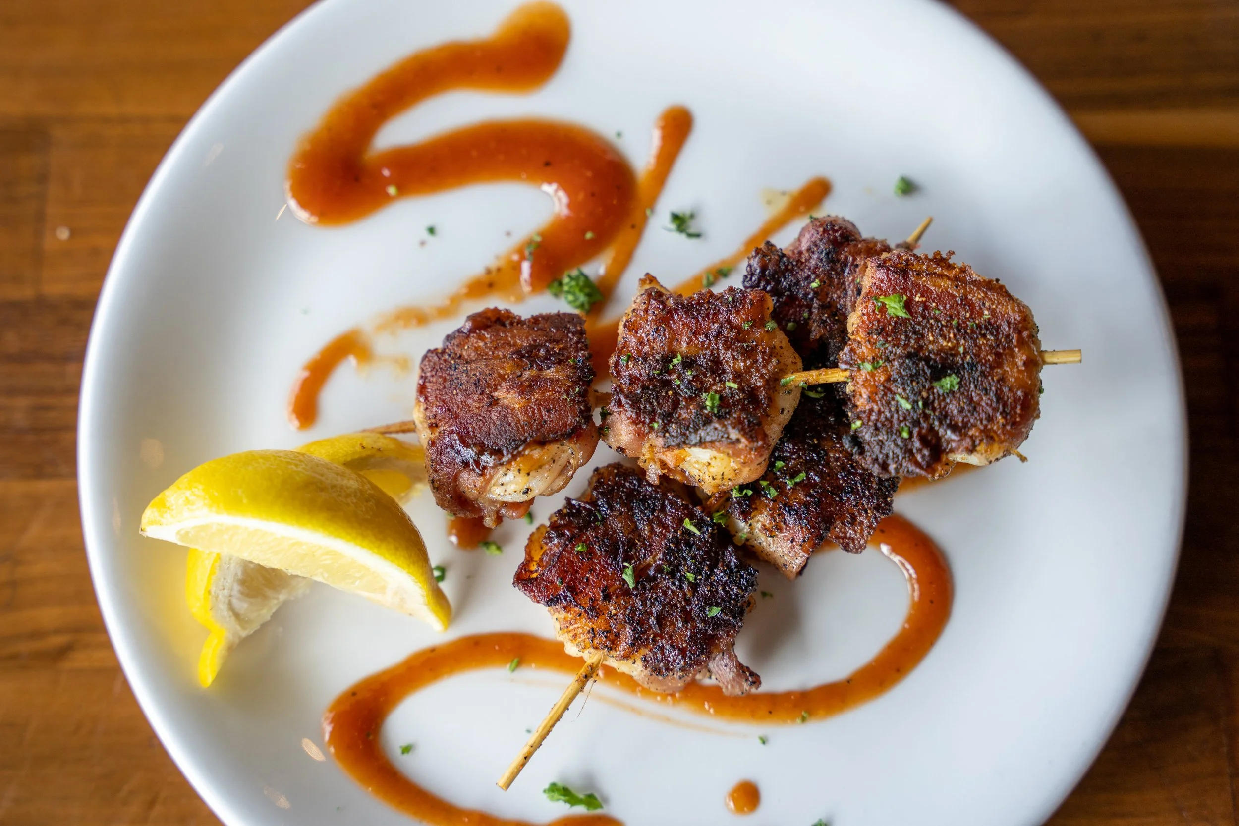 Plate of grilled meat skewers garnished with lemon wedges and drizzled with sauce, served on a white plate.