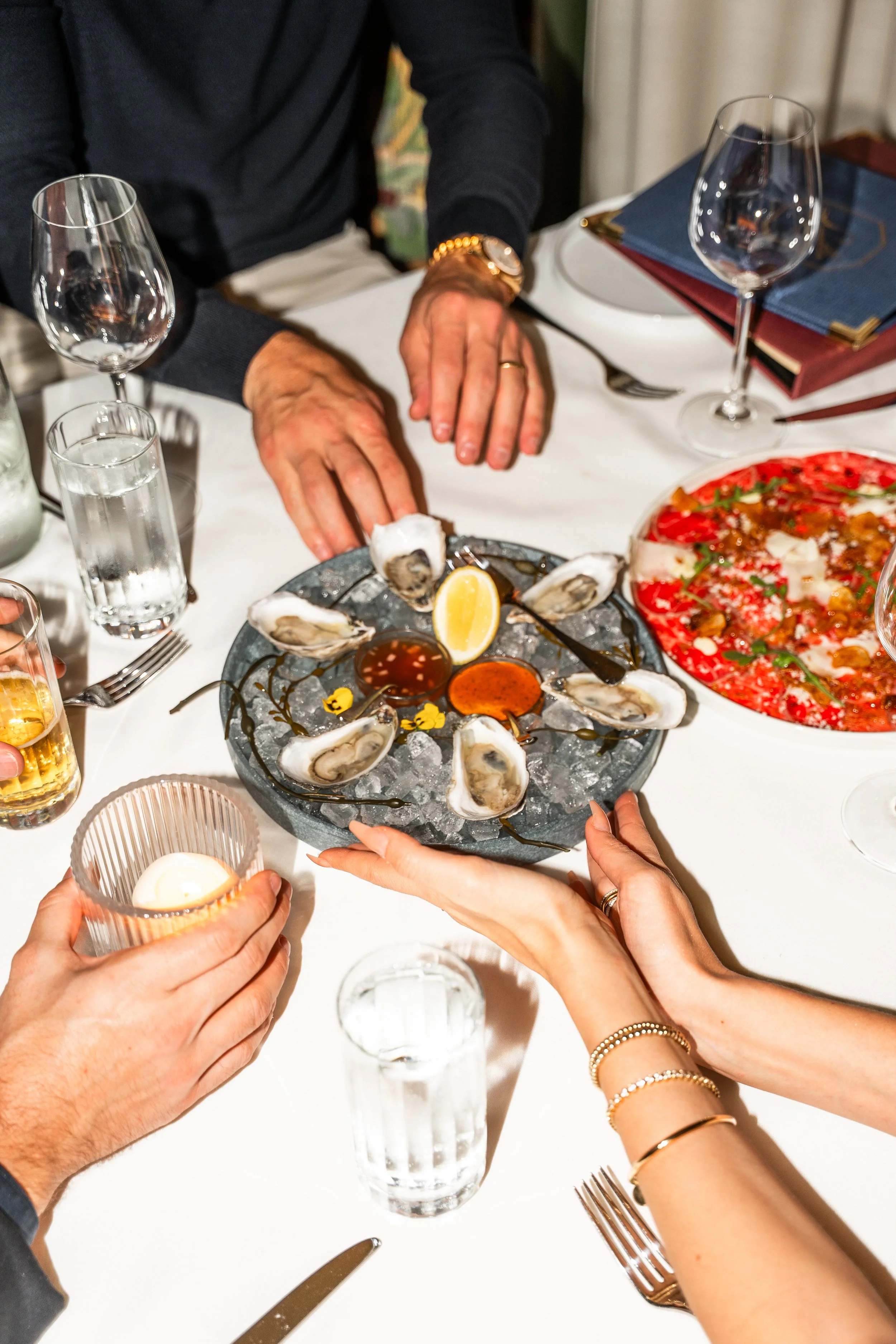 People sharing a seafood meal, including oysters with lemon and sauces, at a dinner table.
