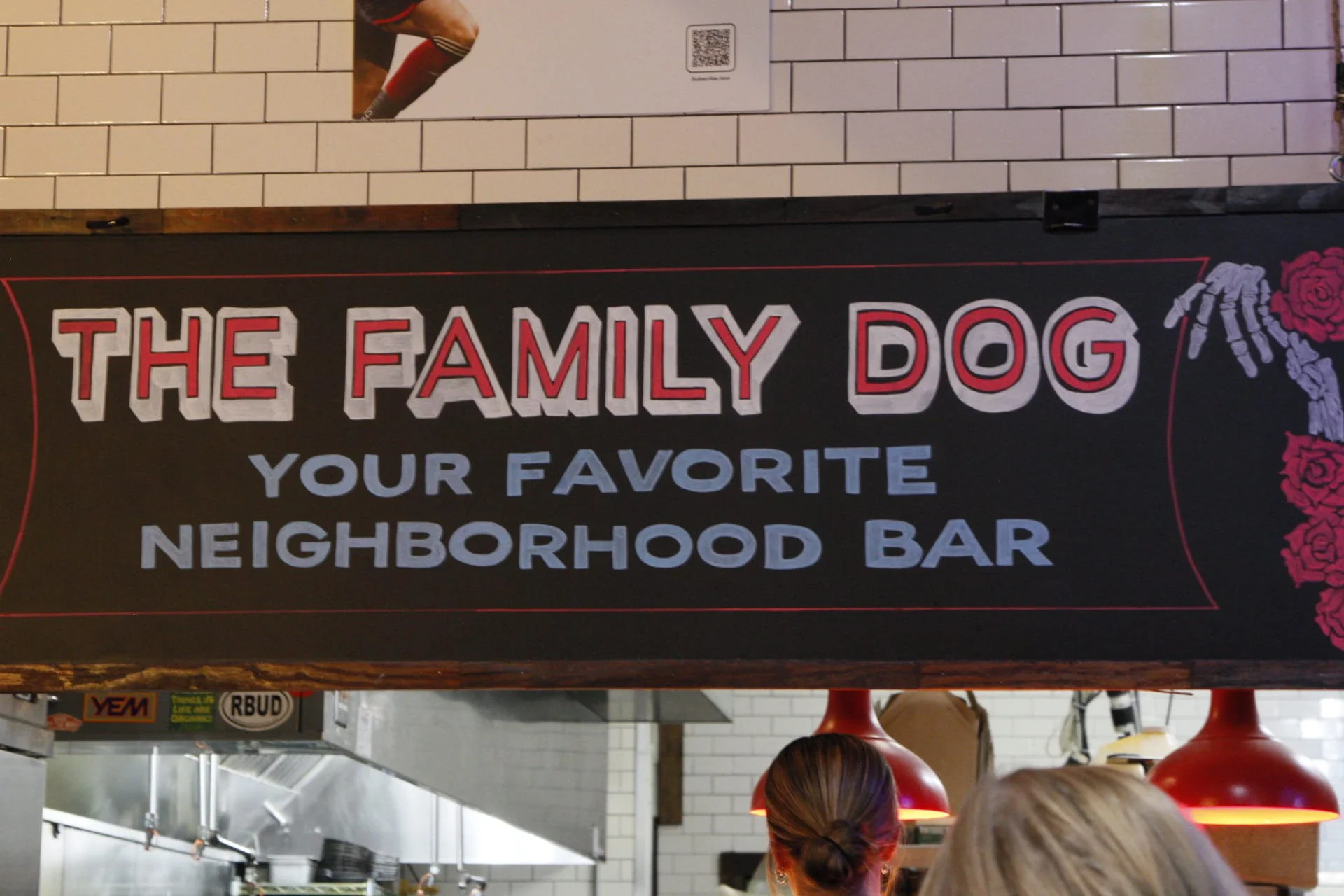 Signboard that reads 'The Family Dog, Your Favorite Neighborhood Bar' with decorative roses and skeletal hand graphics on the edges.
