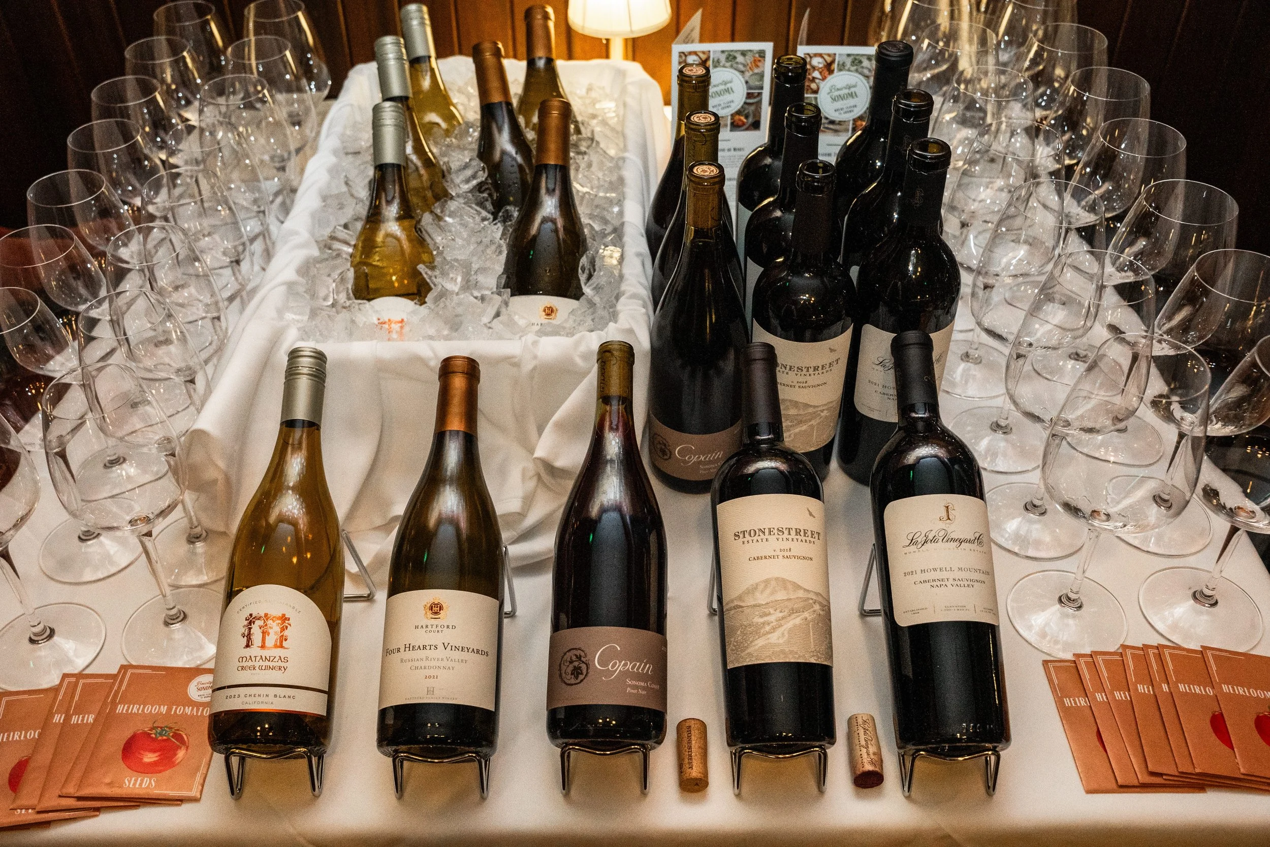 Table displaying bottles of wine with glasses, corks, and seed packets, arranged for tasting or presentation.