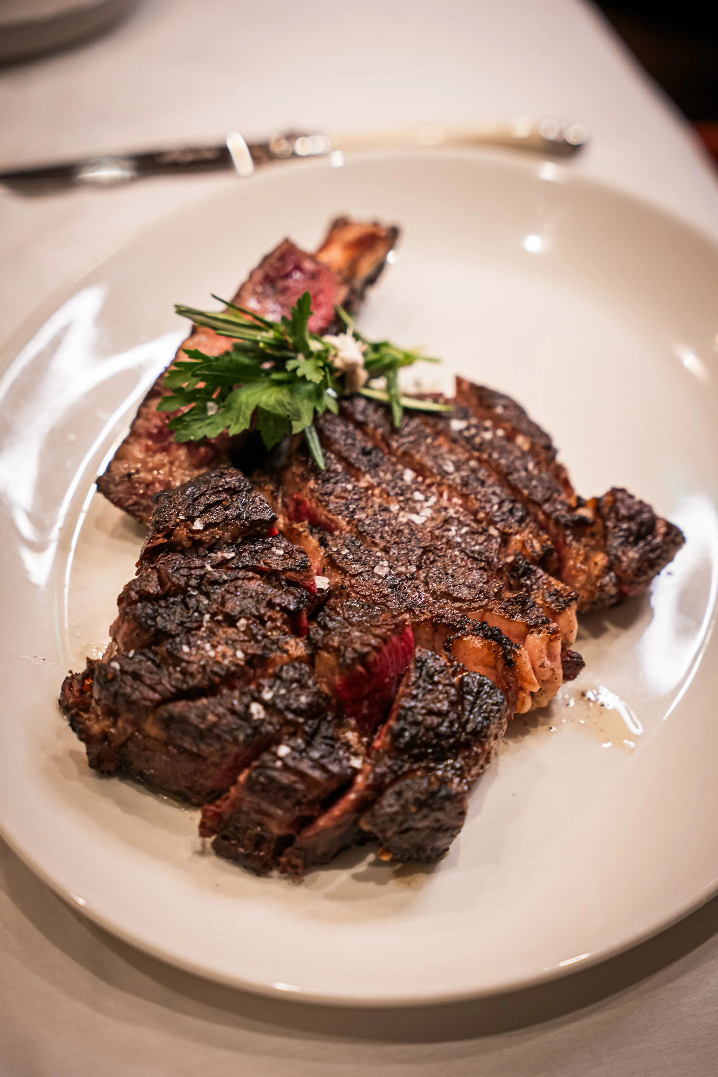 Grilled steak with a sprig of parsley on a white plate.