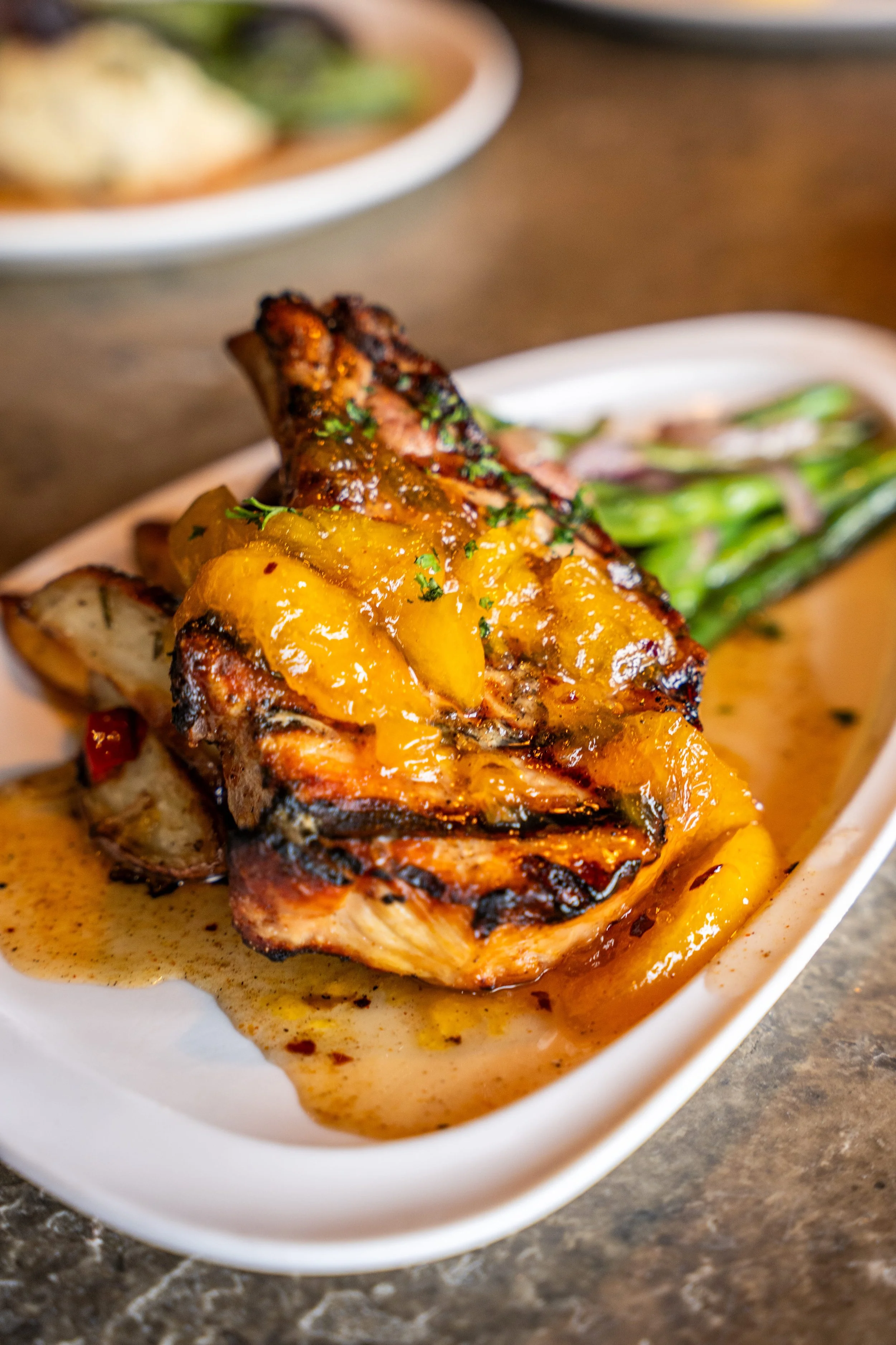 Grilled chicken topped with mango salsa on a white plate, served with roasted vegetables and green beans.