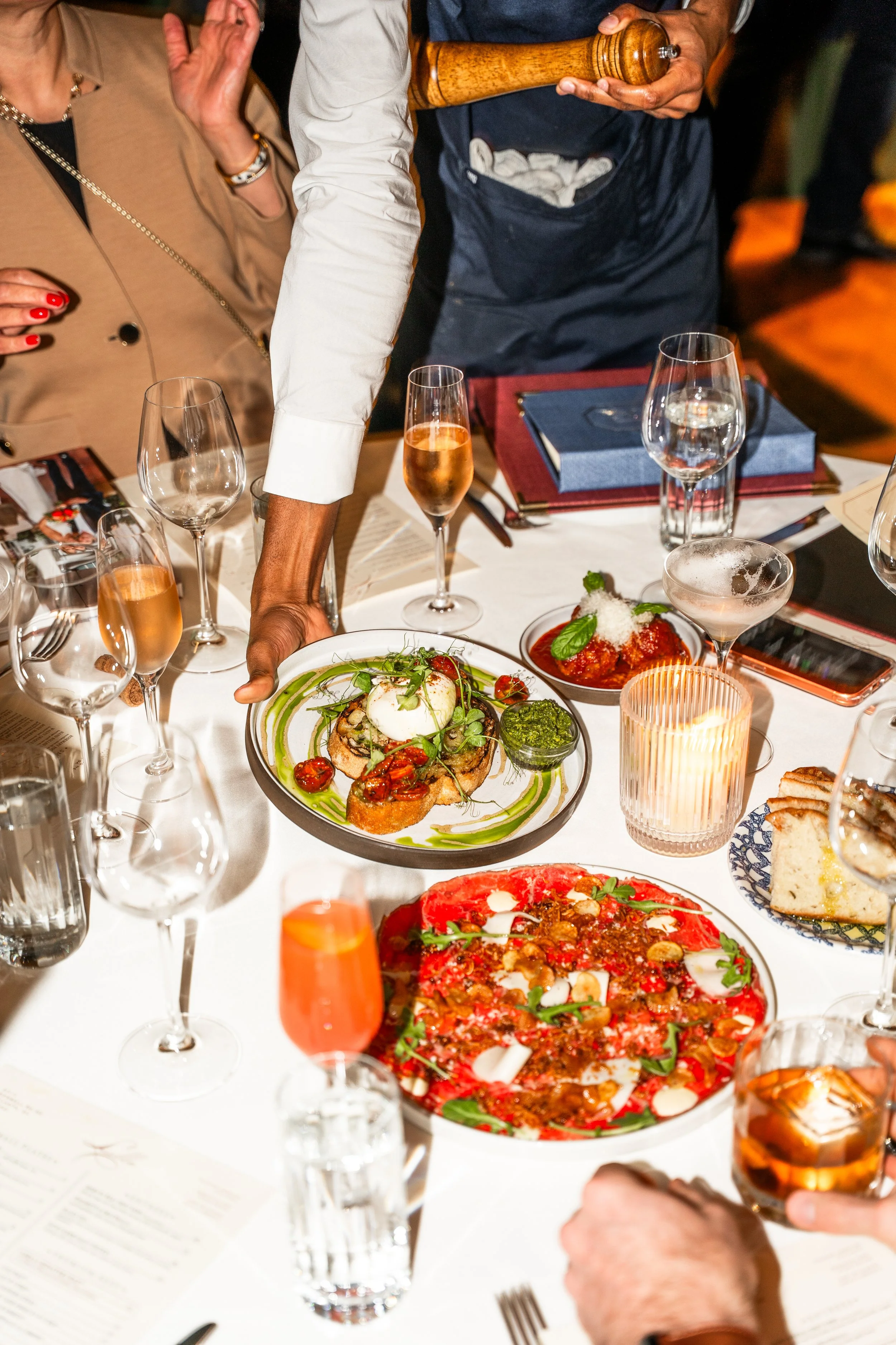 A waiter serving gourmet dishes at a formal dinner event with multiple glasses of wine and water on the table.