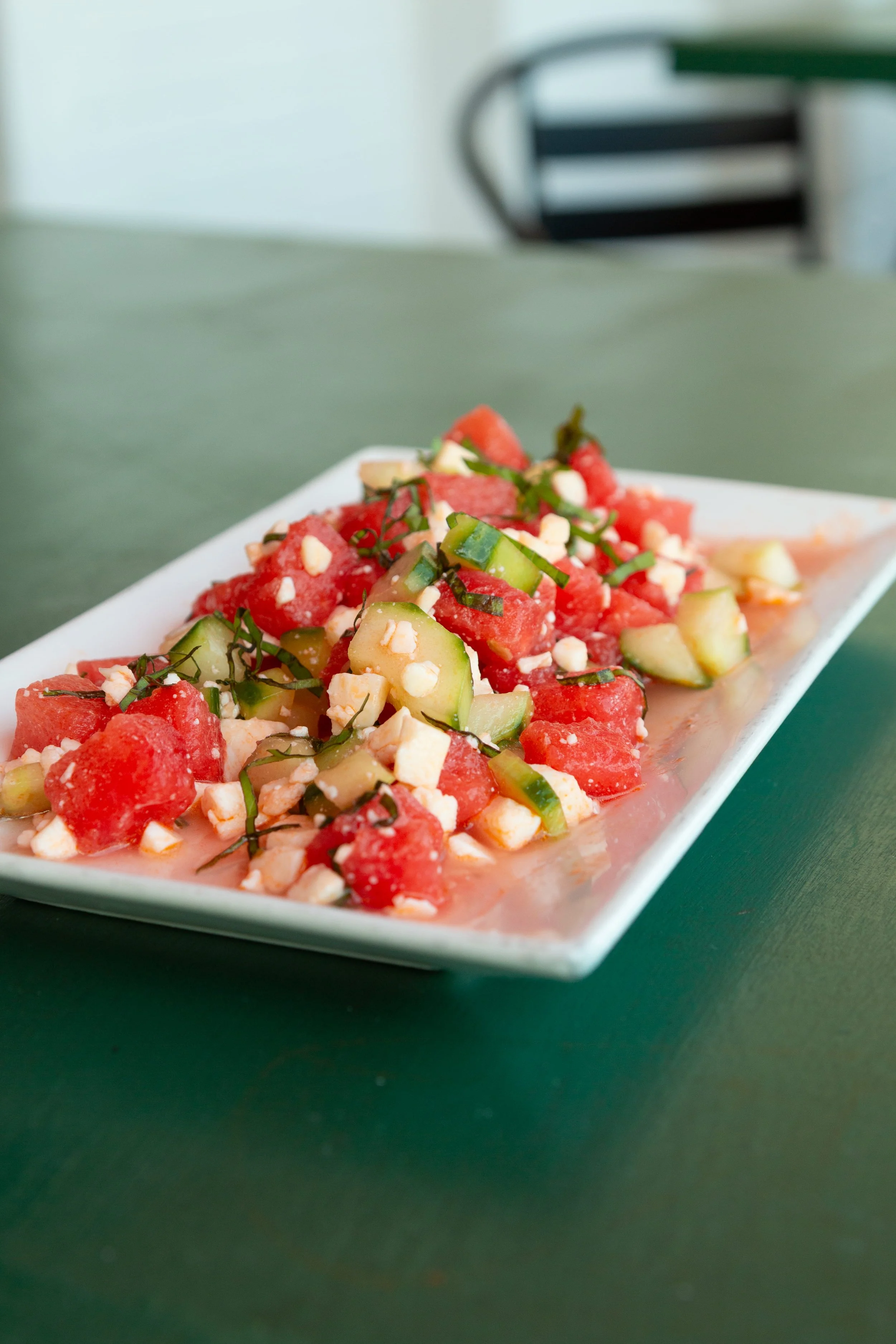 Watermelon and cucumber salad with feta cheese and herbs on a white rectangular plate.