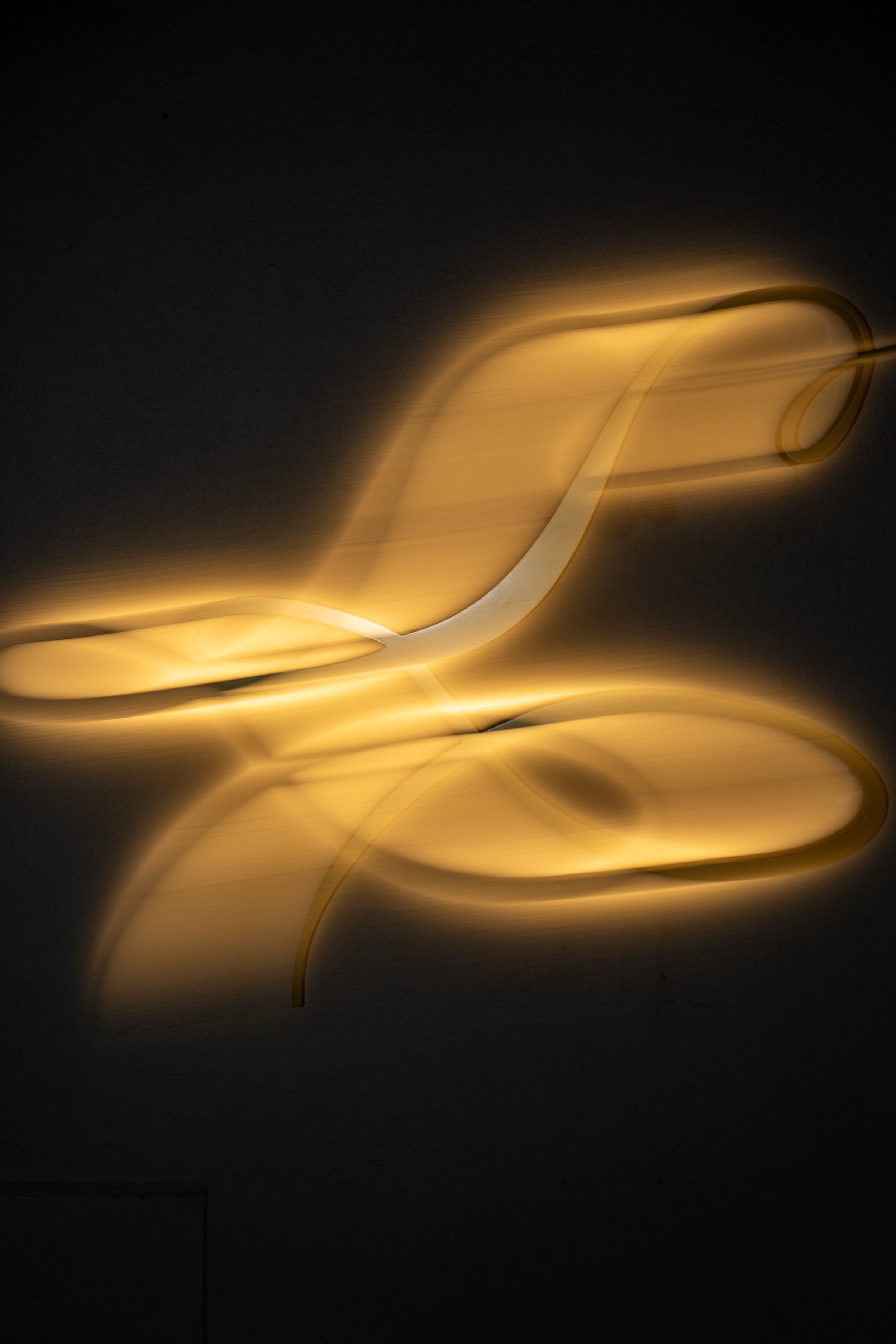Modern gold-colored wall light sculpture with flowing, abstract shapes and a glowing light effect.
