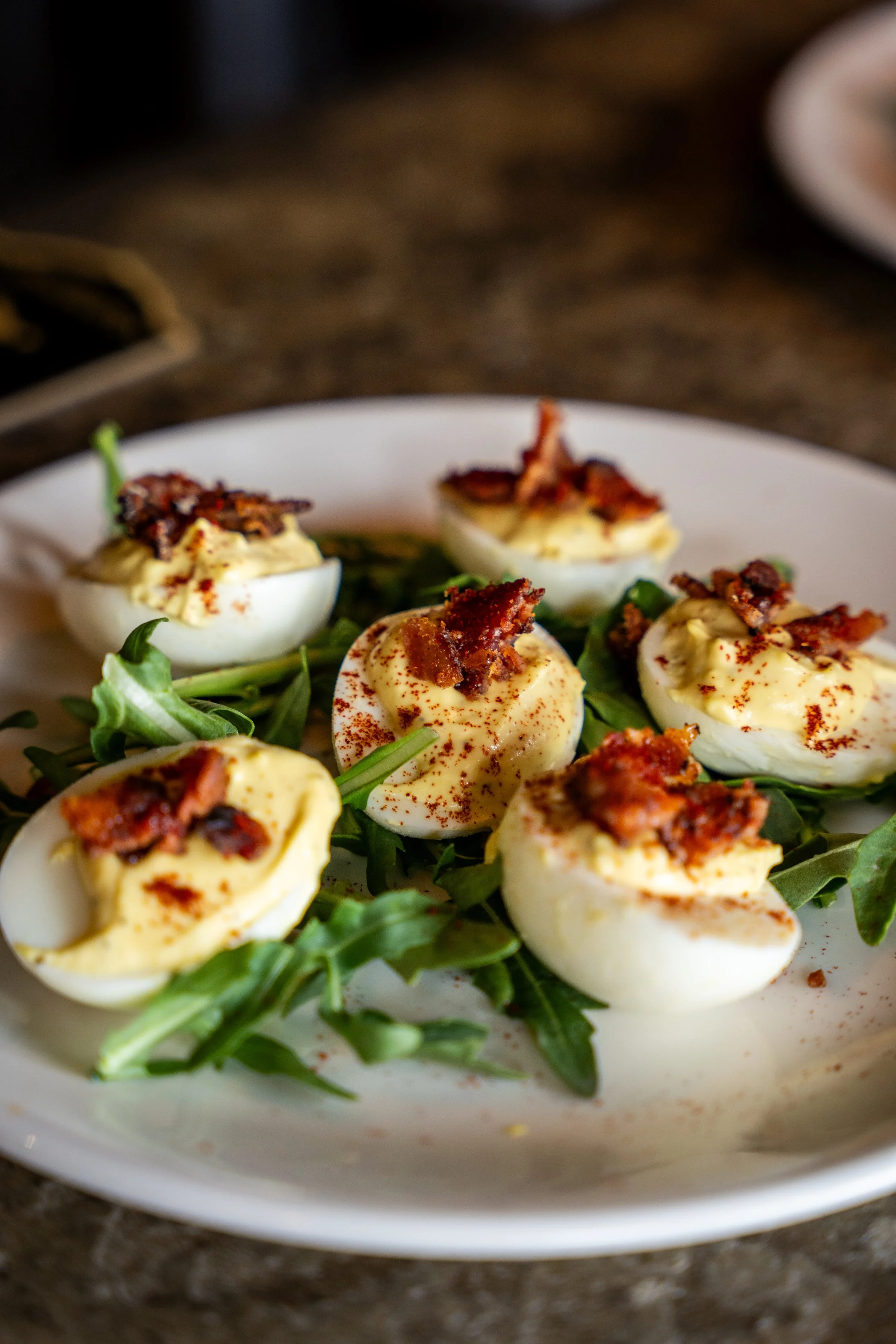 Deviled eggs garnished with bacon bits on a bed of arugula.
