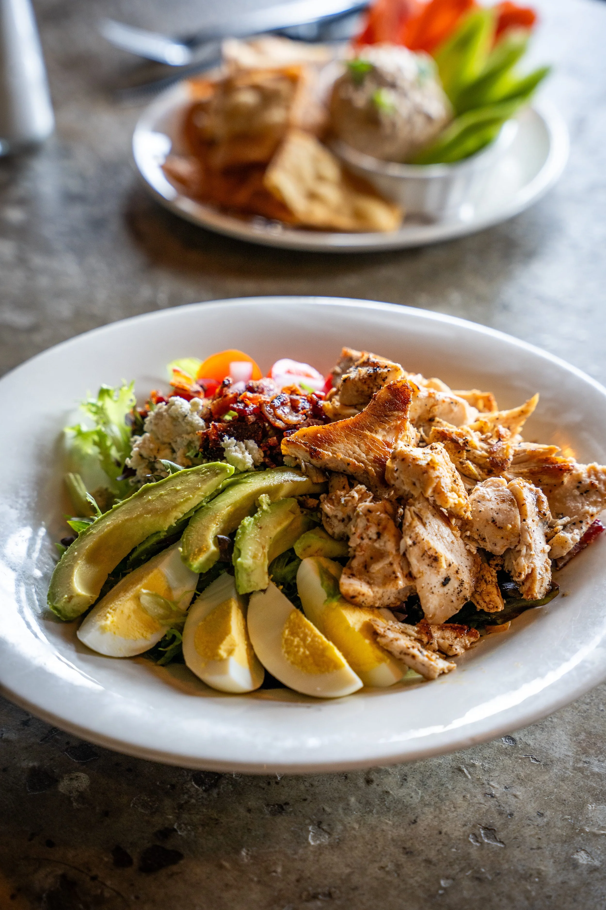 A plate of salad with boiled eggs, avocado slices, grilled chicken strips, cherry tomatoes, and crumbled cheese.
