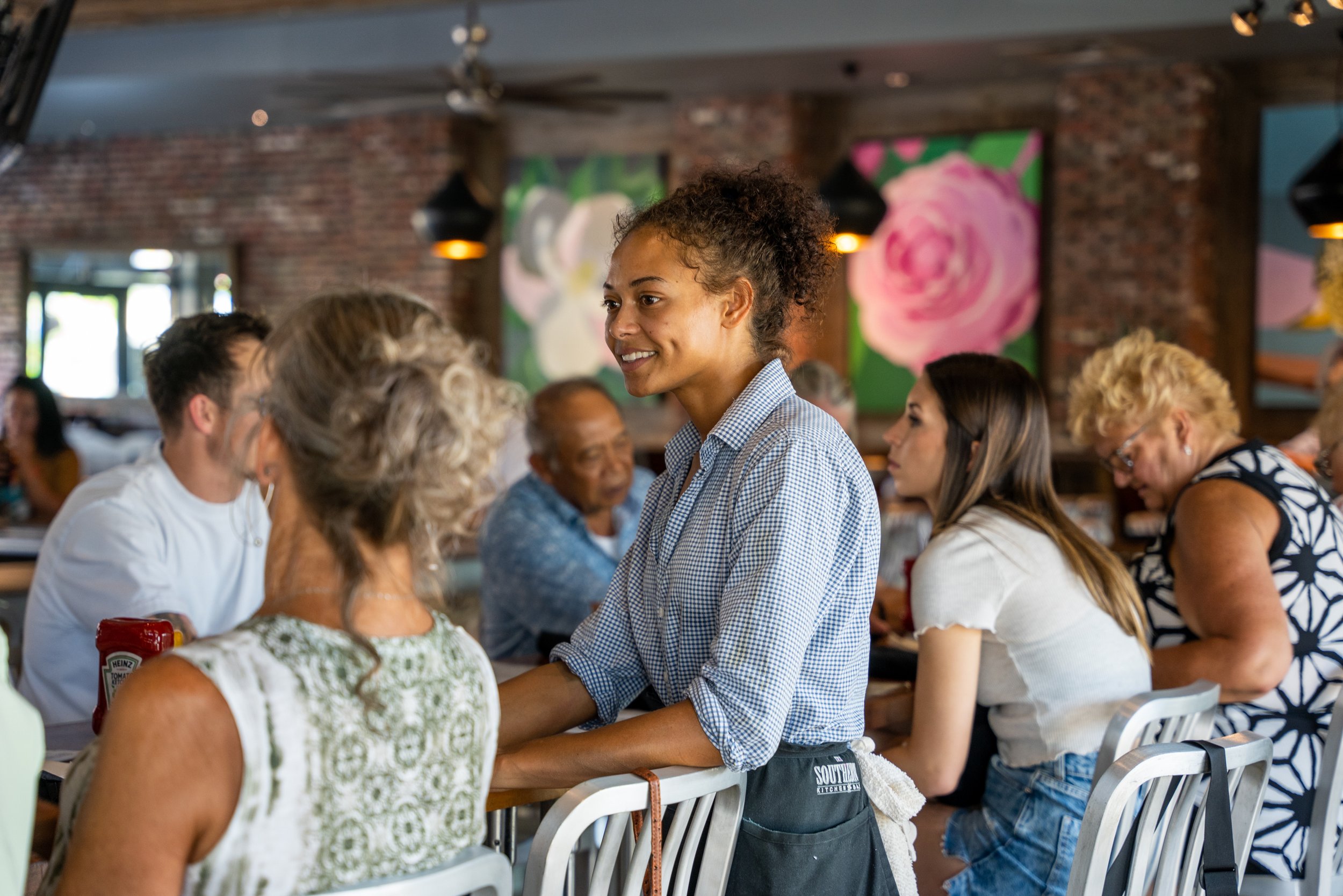 A waitress in a checkered shirt smiling and taking an order from customers at a restaurant.
