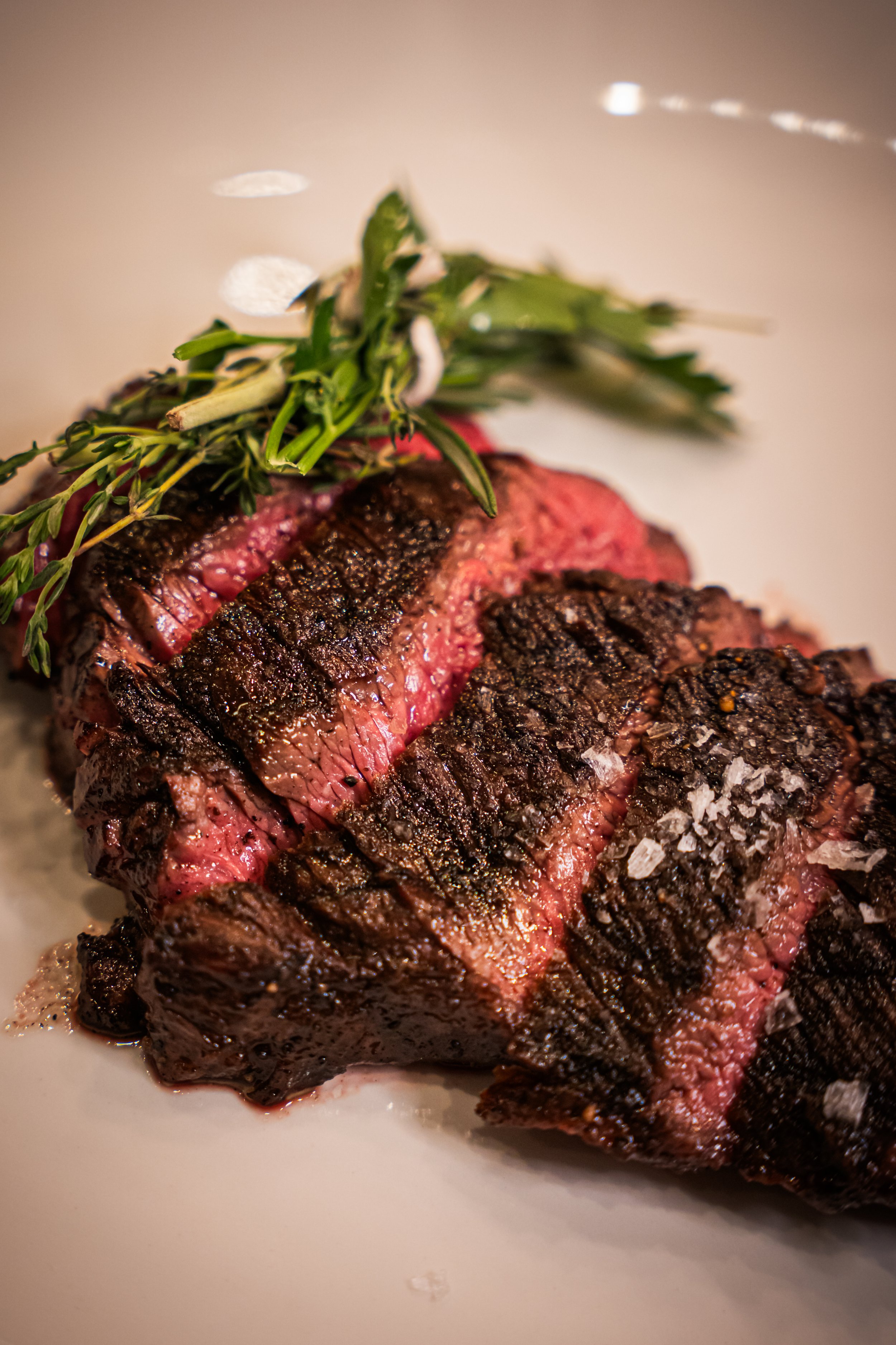 Close-up of sliced cooked steak garnished with herbs on a white plate.