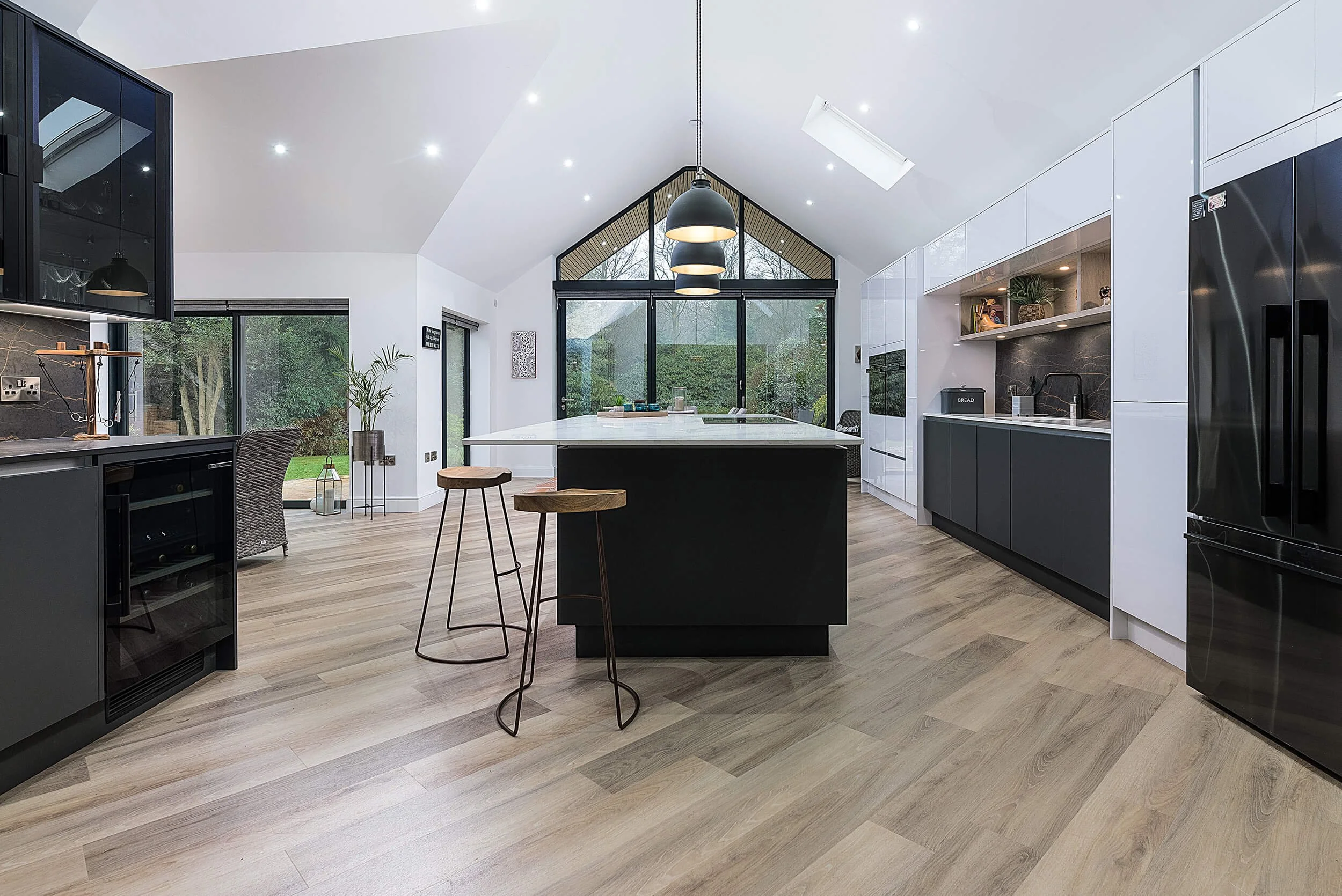 Modern kitchen with black, white, and wooden cabinets, large island with stools, and skylights in a bright, open space.