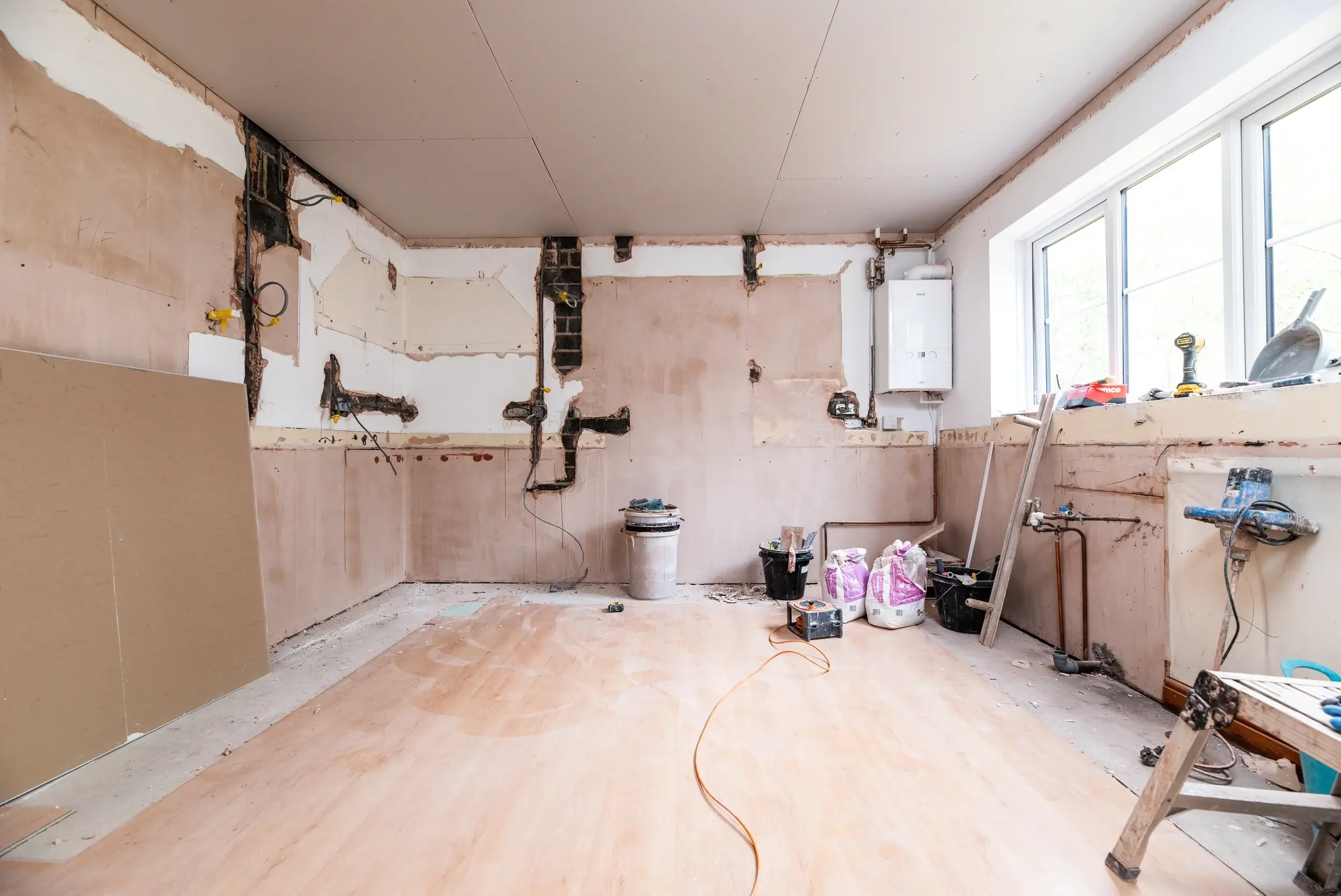 Room under construction with unfinished walls, construction tools, and materials scattered on the floor.