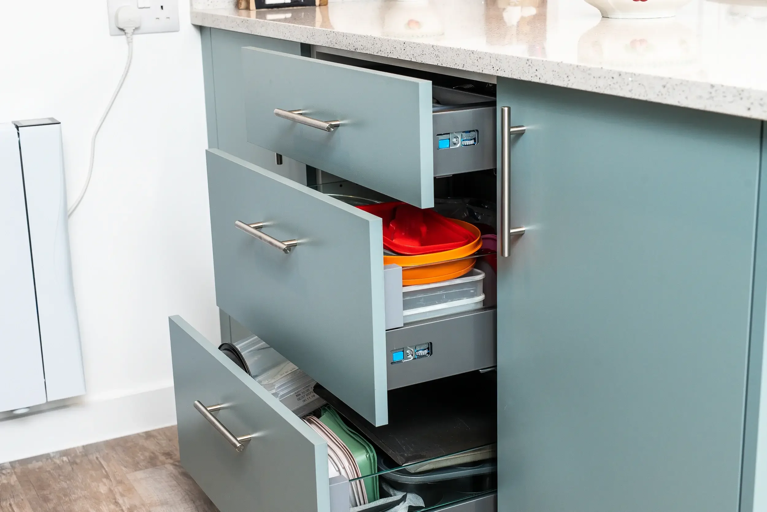 Open kitchen cabinet drawer showing colorful plastic plates, bowls, and other dishware inside.