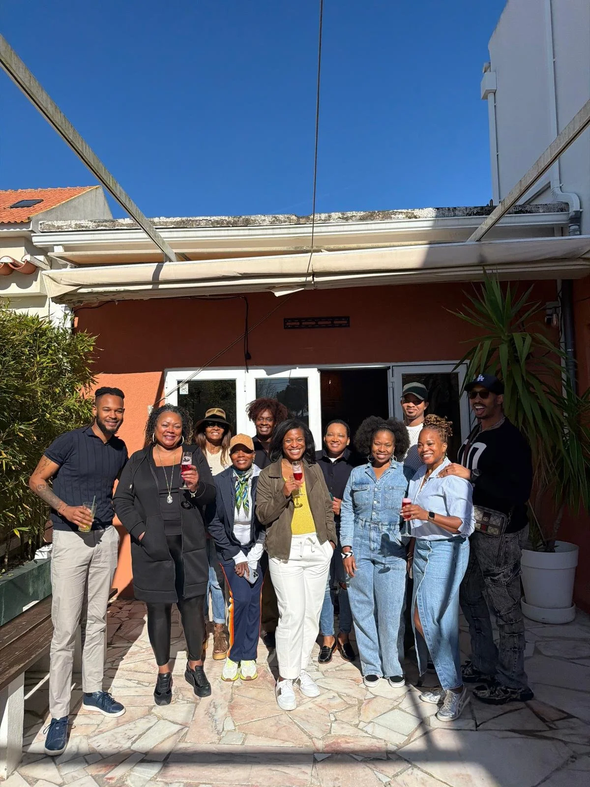 A group of friends stands together on a sunny patio in Lisbon, smiling and holding drinks. The image reflects the community and genuine friendships Jacinta built during her first year living in Portugal.