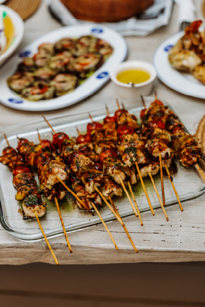 Skewers of grilled chicken and vegetables on a glass platter, with other dishes and dipping sauces in the background.