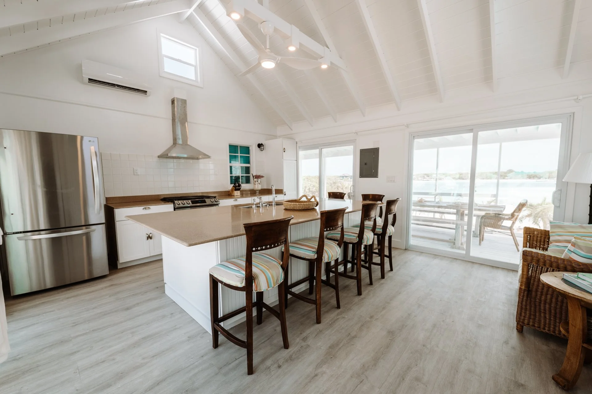 Bright kitchen with white walls, a wooden island with chair seating, stainless steel refrigerator, white cabinetry, and a view of the patio through large sliding glass doors.