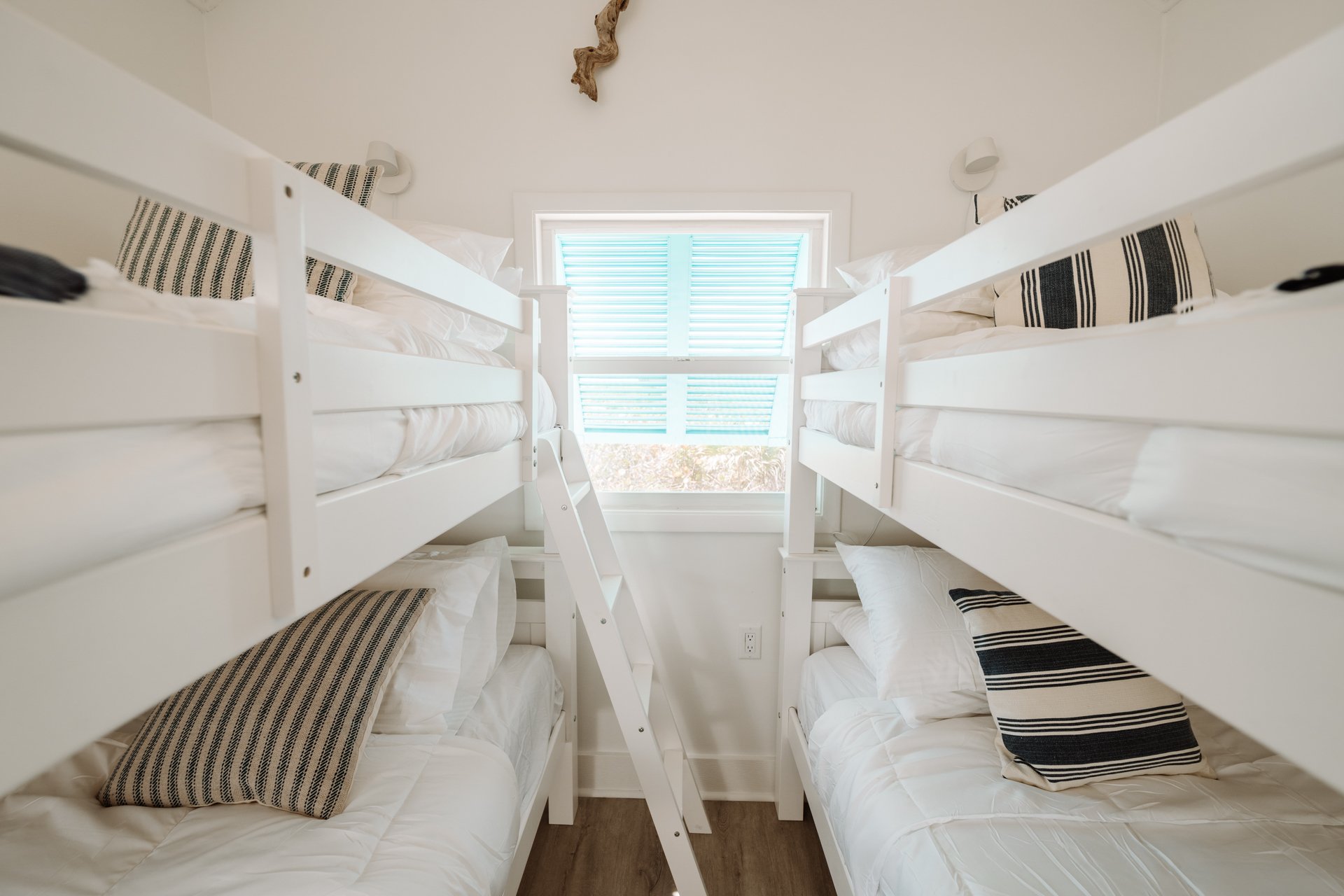 Room with four white bunk beds, two on each side, and a window with blue blinds in the center.