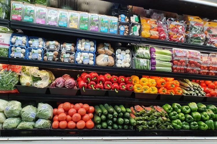 Fresh vegetables and packaged produce on store shelves, including lettuce, tomatoes, cucumbers, bell peppers, and mushrooms.