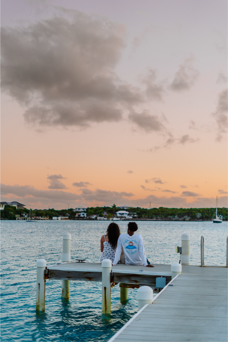 A couple sitting on a wooden dock by the water during sunset.