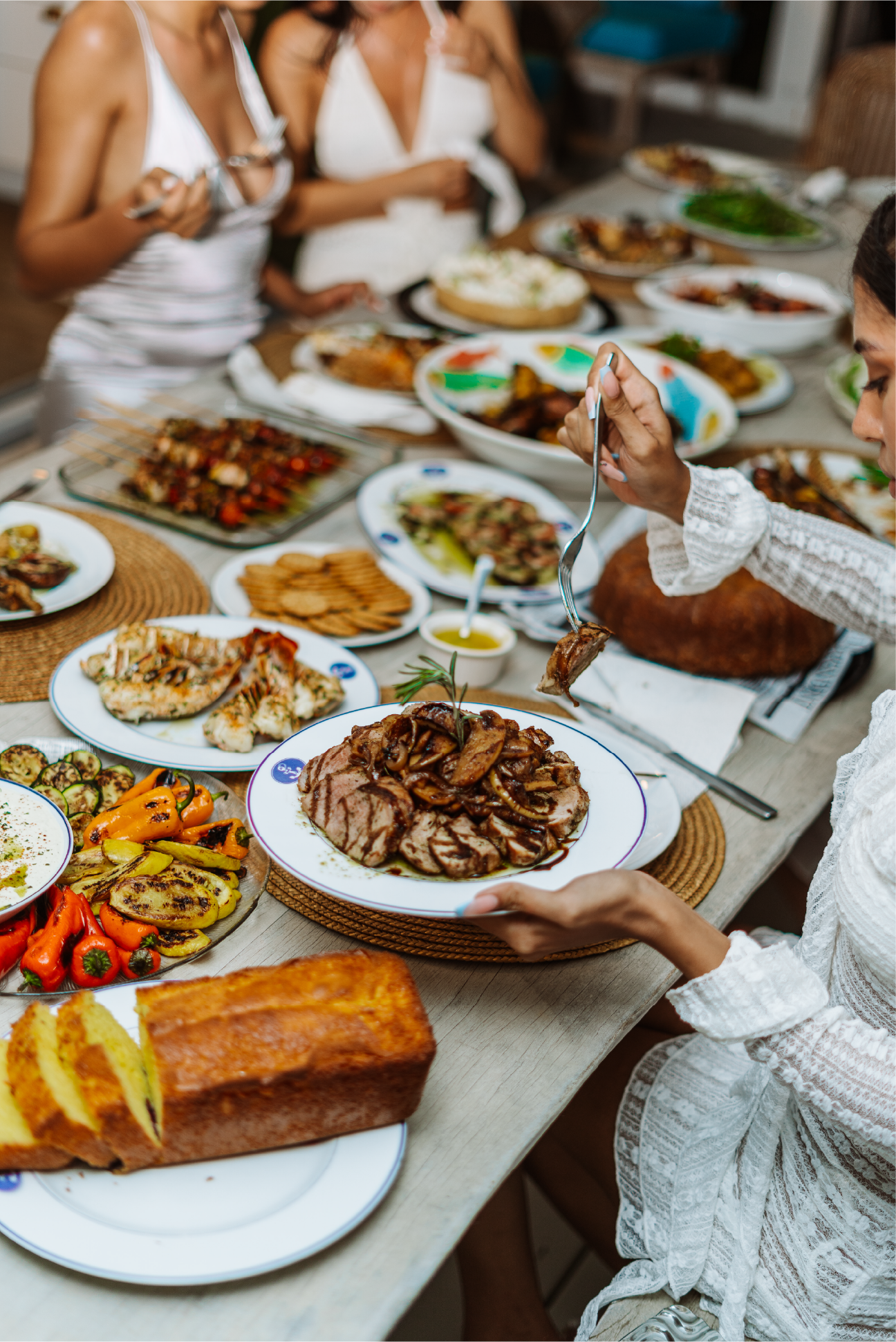 A woman in a white dress preparing to serve herself at a table full of various dishes during a gathering or celebration.