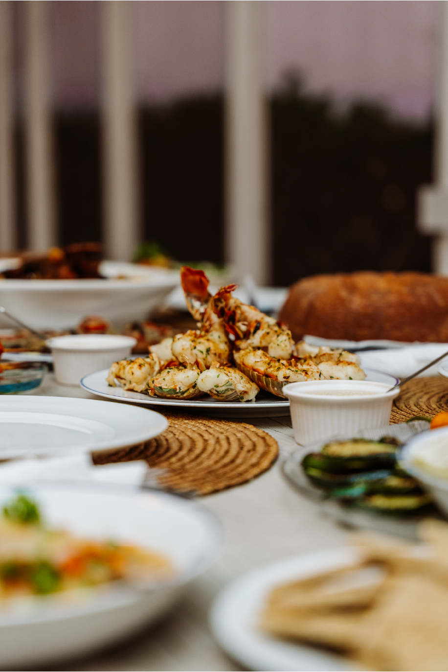 A table of seafood dishes, including grilled shrimp, clams, and other items, set on a table with woven placemats, with some small bowls of dipping sauces or sides.