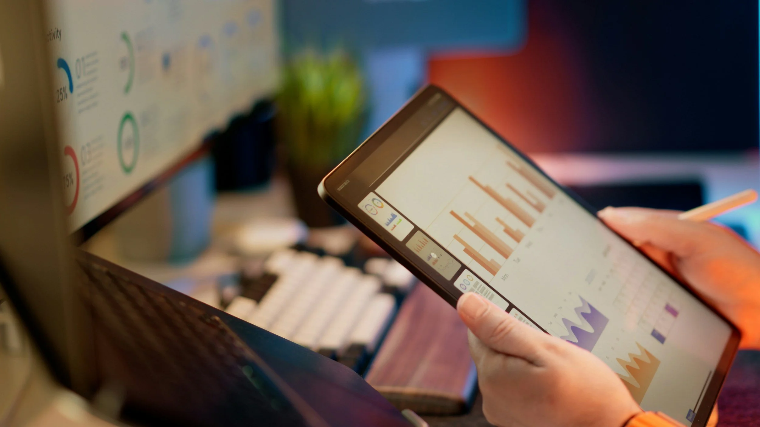 Person holding a tablet with colorful bar and line graphs displayed on the screen, in an office or workspace environment.