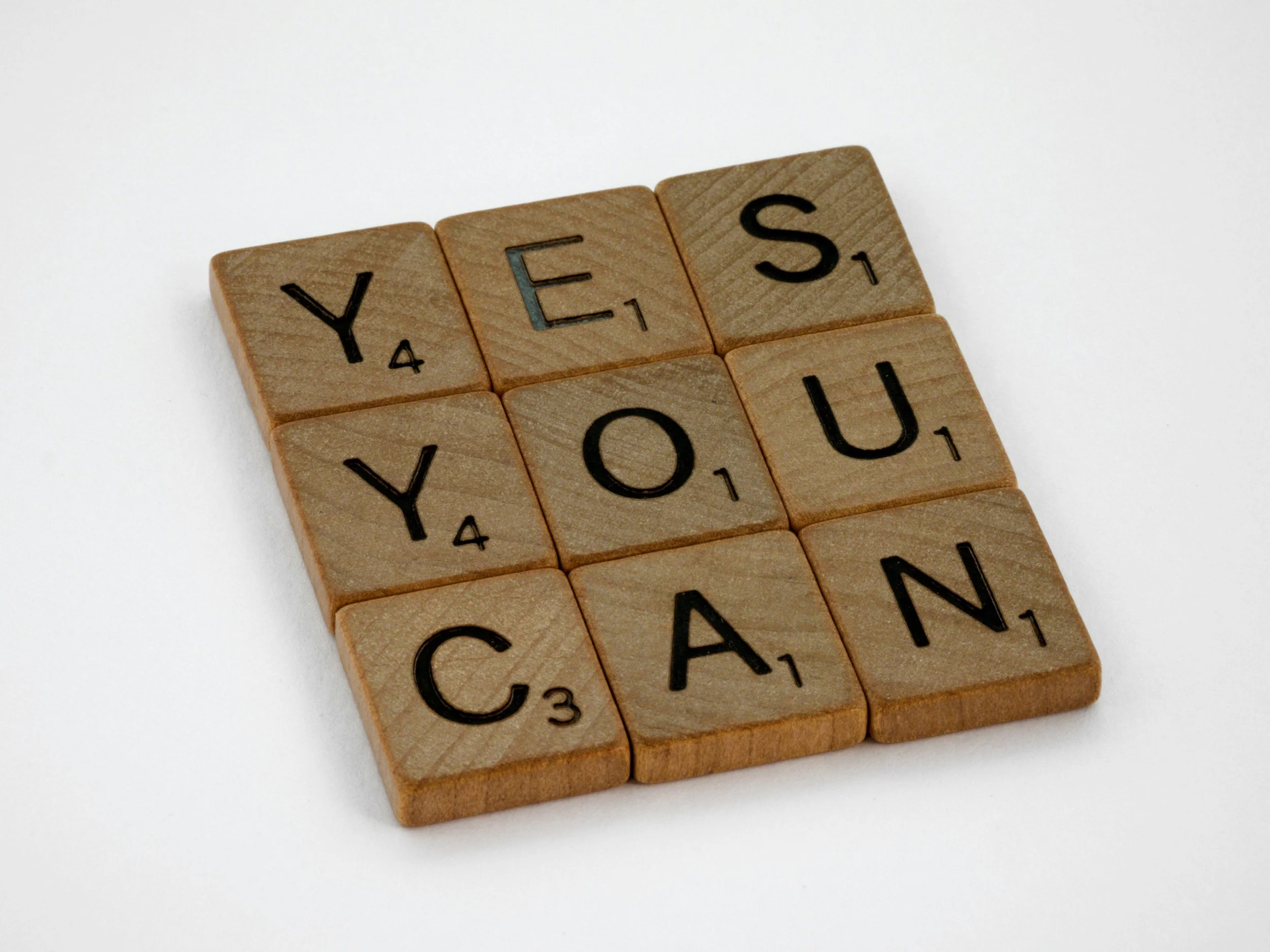 Scrabble tiles spelling out 'YES YOU CAN' on a white background.