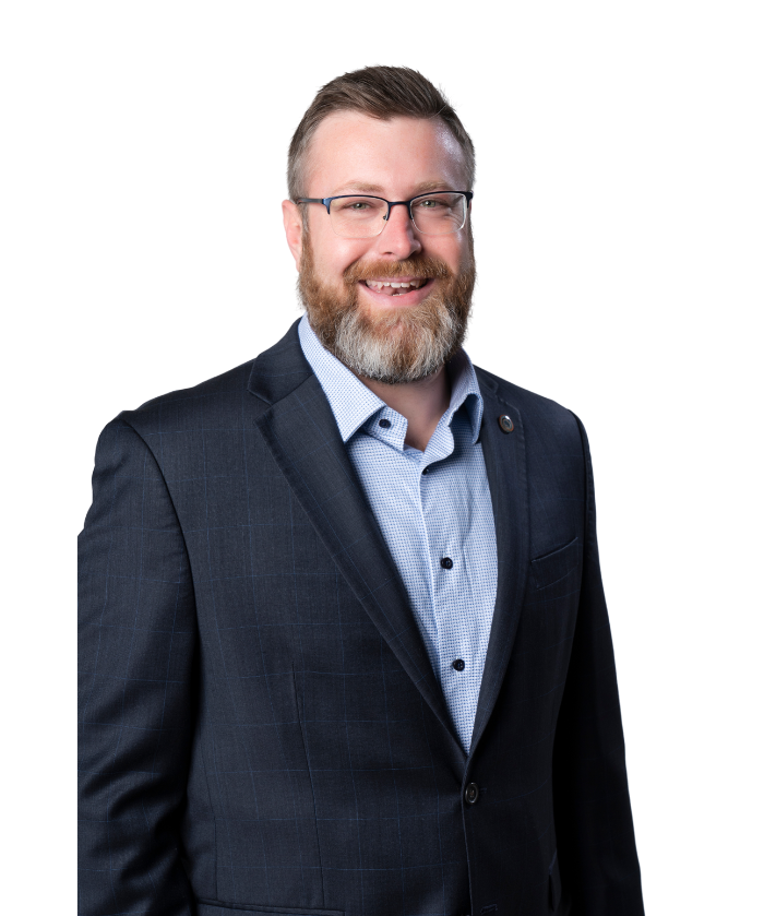 A smiling man with glasses, a beard, and short hair wearing a dark blazer and light blue shirt against a white background.