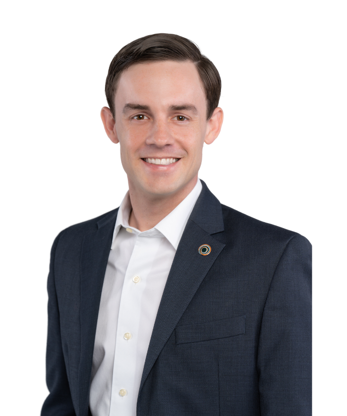 A young man with short dark hair and fair skin wearing a navy blazer and white dress shirt, smiling at the camera against a plain white background.