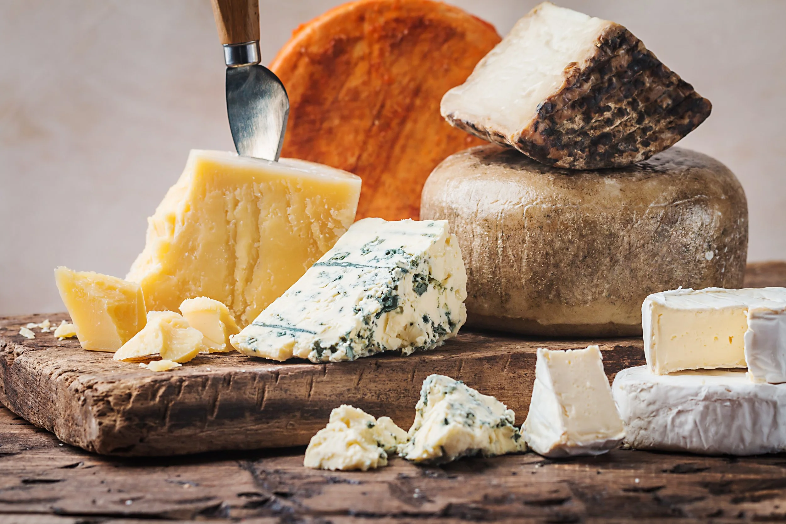 Various types of cheese on wooden surface, including blue cheese, brie, cheddar, and aged cheese, some with a cheese knife.