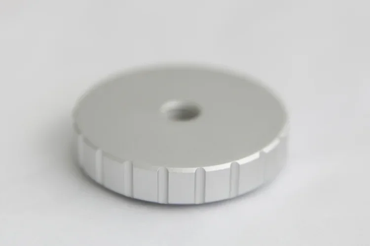 A white and silver round plastic spool or reel with a central hole, placed on a white surface.