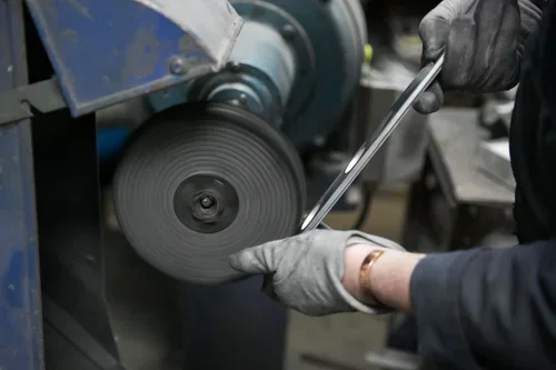 Person using a metal file to smooth a metal surface on a machine in a workshop.