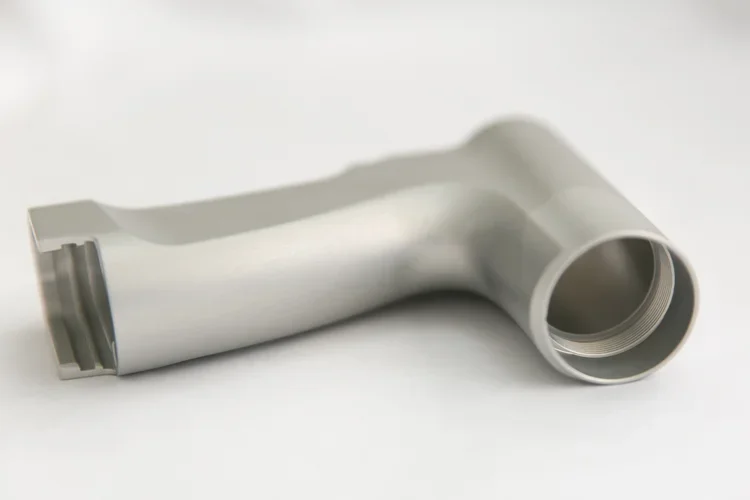 A silver metallic pipe fitting with a 90-degree bend lying on a white surface.