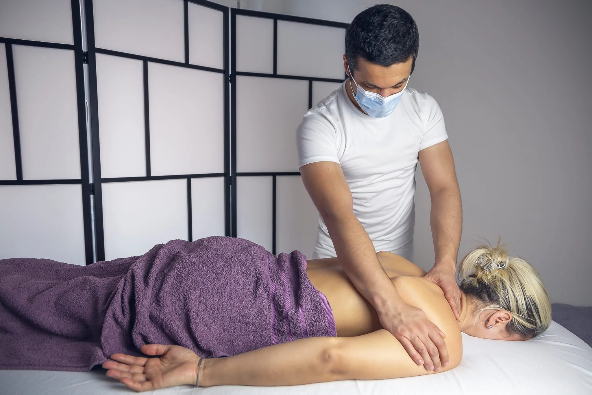 Masseur gibt einer Frau eine Rückenmassage in einem Behandlungsraum